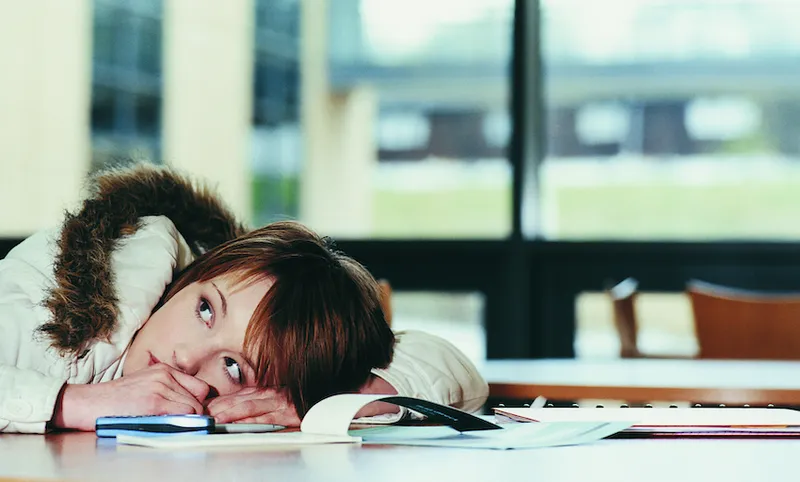 Worried Female University Student With Her Head on a Table Next to a Cheque Book