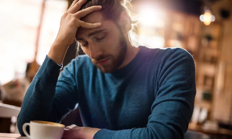 Stressed man holding his head in pain in a cafe.