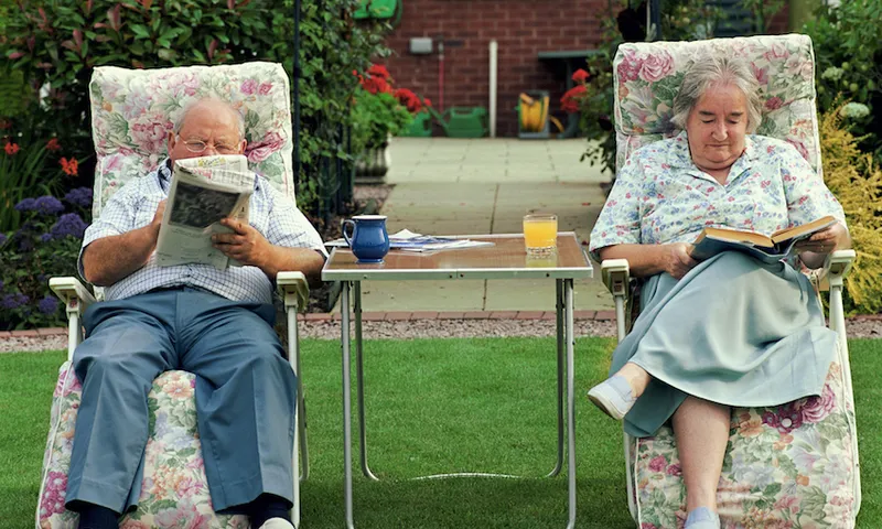 Wonderful old couple reading on lawn chais, a wee table in between them, on a lawn