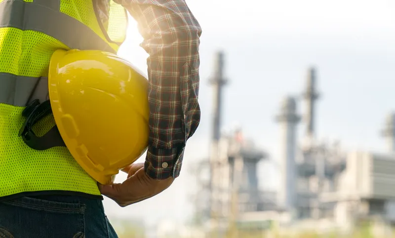 engineering man with white safety helmet standing in front of oil refinery building structure in heavy petrochemical industry