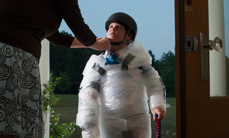 Mother putting helmet on son’s (10-11) head wrapped in bubble wrap