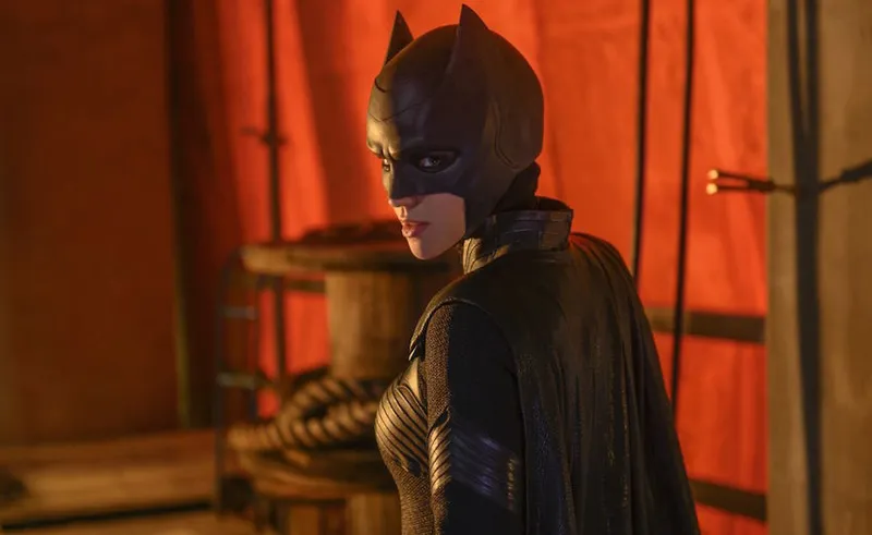 Batwoman, without a wig, looks mysteriously over her shoulder in a red-lit room