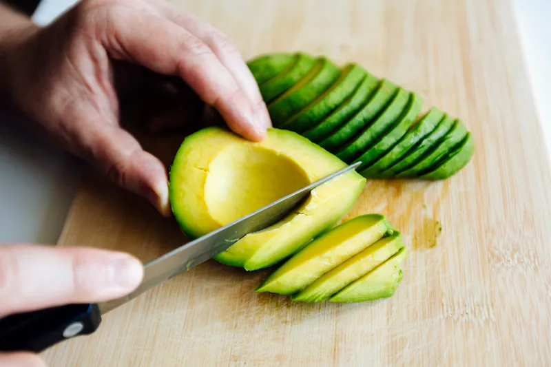 Man slicing avocado with a knife on a cutting board close up