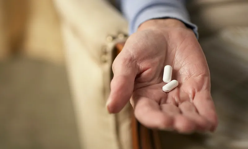Senior woman holding two pills, close-up of hand