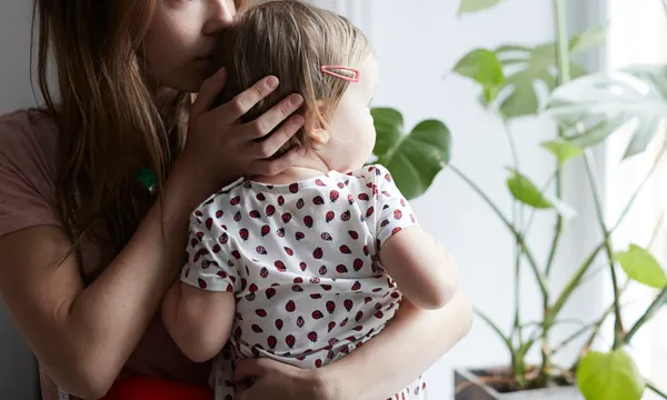 Mother kissing daughter while looking through window at home