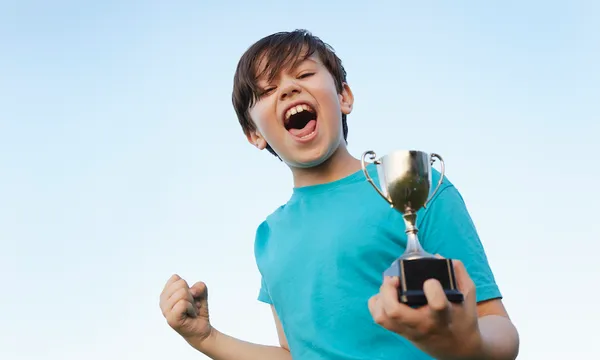 Boy making fist and holding sport trophy against blue sky