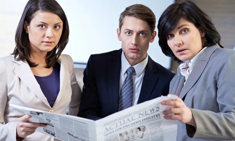 Business colleagues holding newspaper and looking at camera with surprise