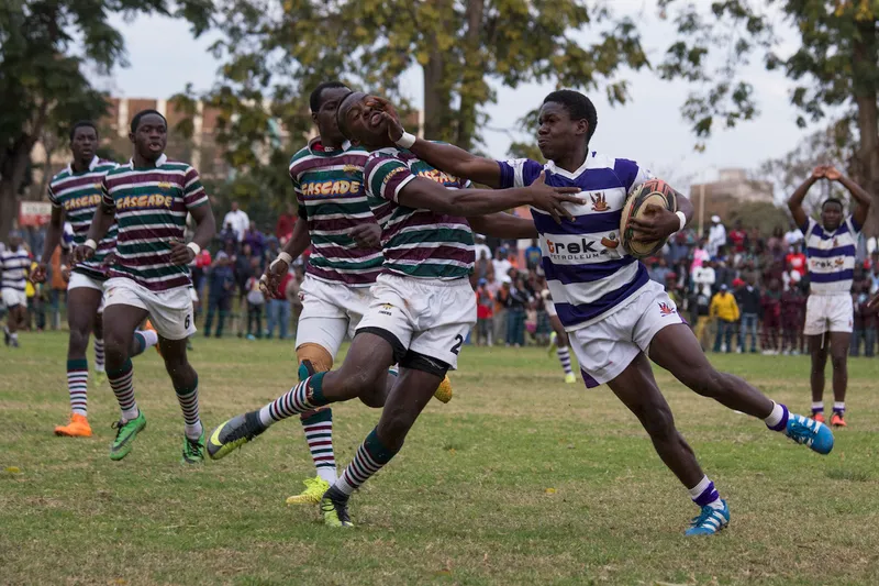 A Prince Edward School (green, maroon and white stripes) player is fended off by Churchill High School player, Albert...