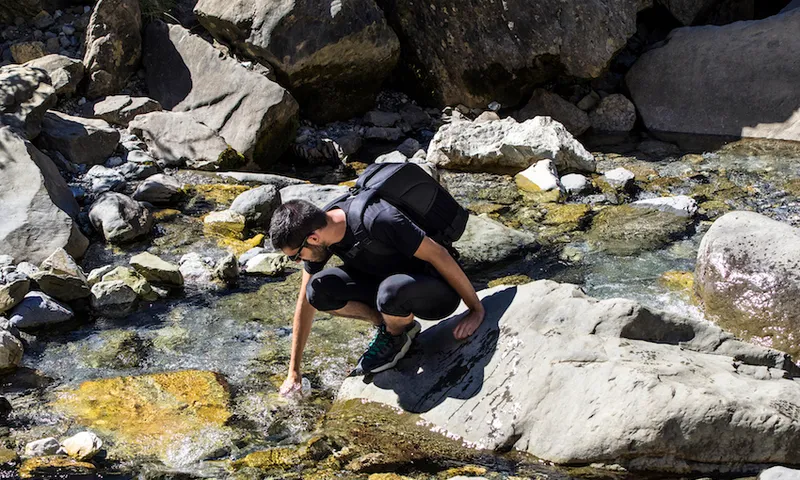 Tripper filling a water bottle in a river of high mountain