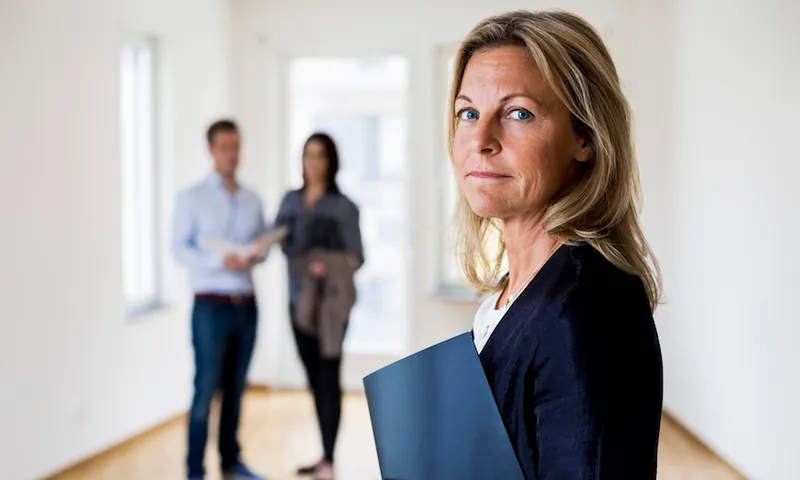 female real estate agent with couple standing in background at home