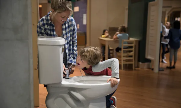Mother and son drinking from toilet water fountain in science center