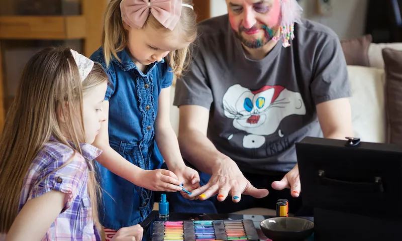 Two children painting their father’s fingernails
