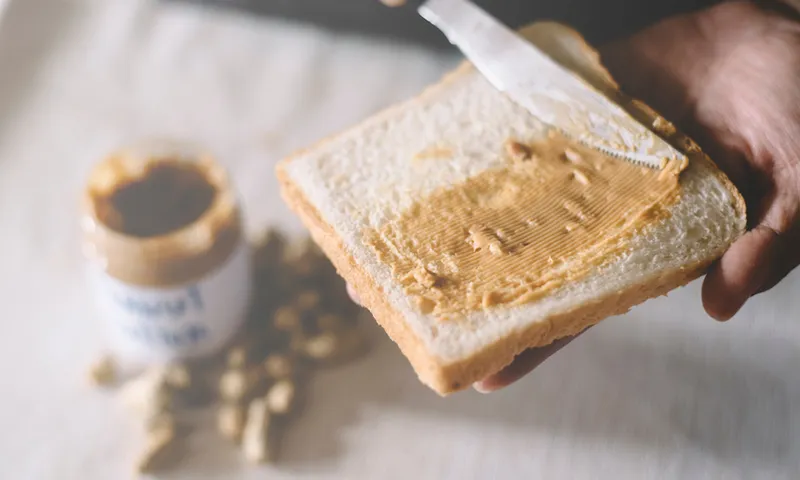 Close-Up Of Person Applying Peanut Butter On Bread On Table