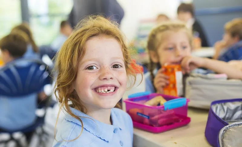 Smiling Girl Missing a Tooth With a Healthy Lunch