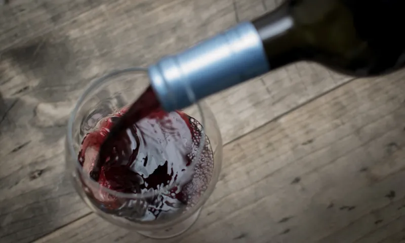 Close-Up Of Red Wine Pouring From Bottle In Glass On Table