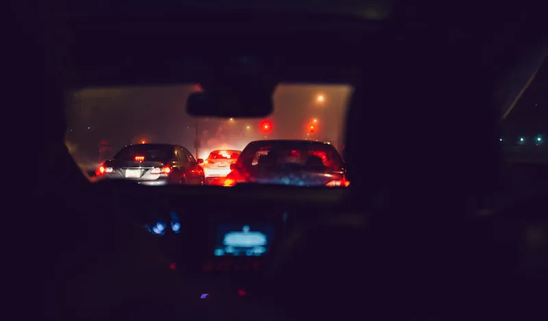 Night time busy street view with illuminated car lights seen through car windshield at traffic jam