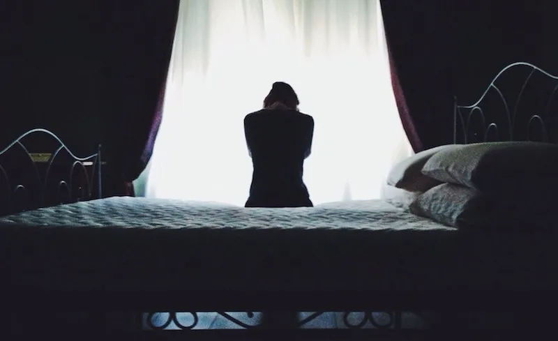 Rear View Of Woman Sitting On Bed Against Curtain