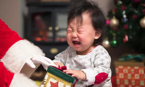 Cropped Hands Of Santa Claus Giving Gift To Crying Baby Girl