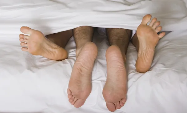 High angle view of a couple’s feet under the sheets of a bed