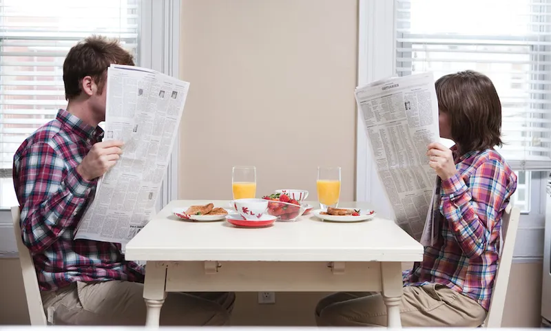 Young couple reading newspapers at kitchen table