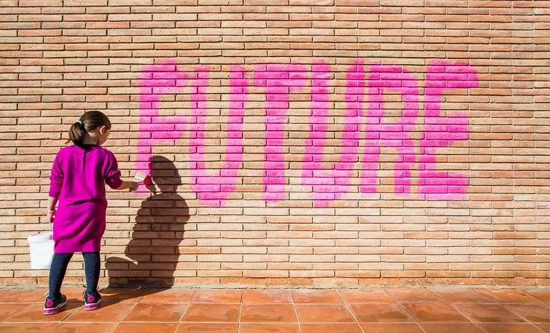 Little girl painting with pink colors the future word in a brick wall, a protest action claiming for future to the new generations.