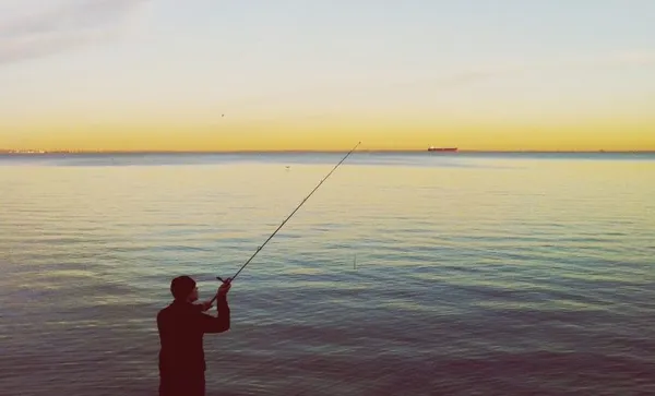 Rear View Of Man Fishing In Lake Against Sky