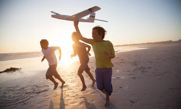 Boys running along beach with a toy plane