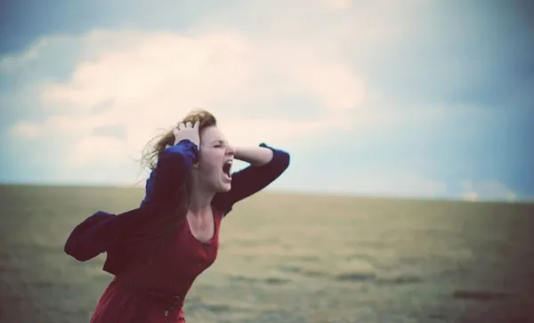 Young woman screaming in windy, cloudy field
