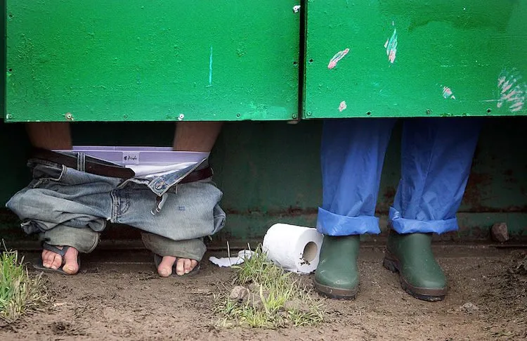 Two festival-goers pass a roll of toilet paper between toilet cubicles, during the 2004 Glastonbury Festival. (Photo: Matt Cardy/Getty Images)