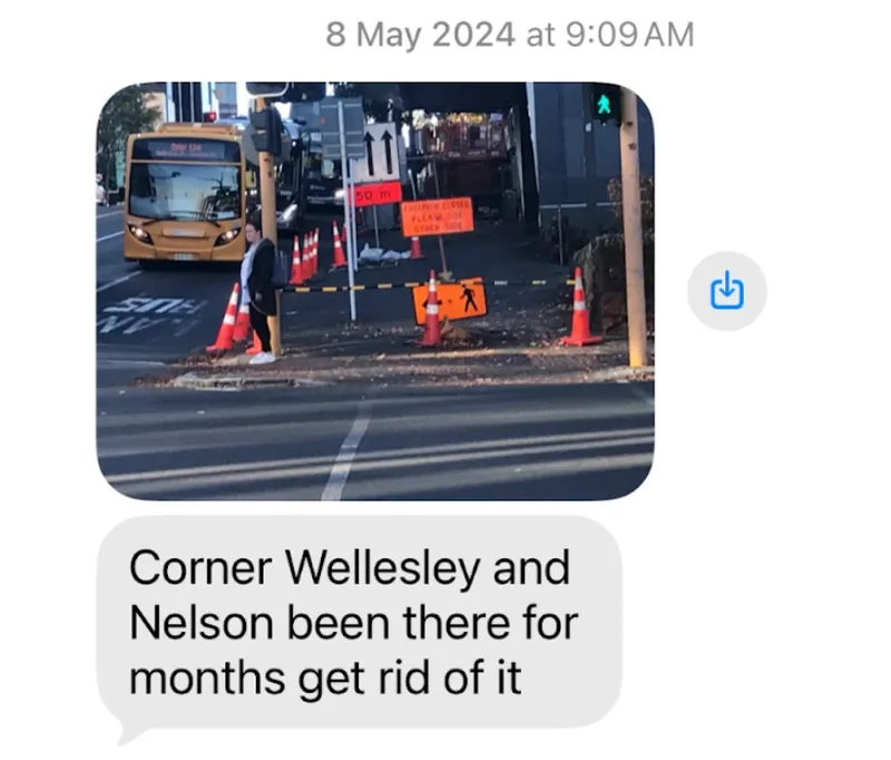 A street corner with orange construction cones, a bus, a pedestrian, and a sign blocking part of the sidewalk. A message below says, "Corner Wellesley and Nelson been there for months get rid of it.