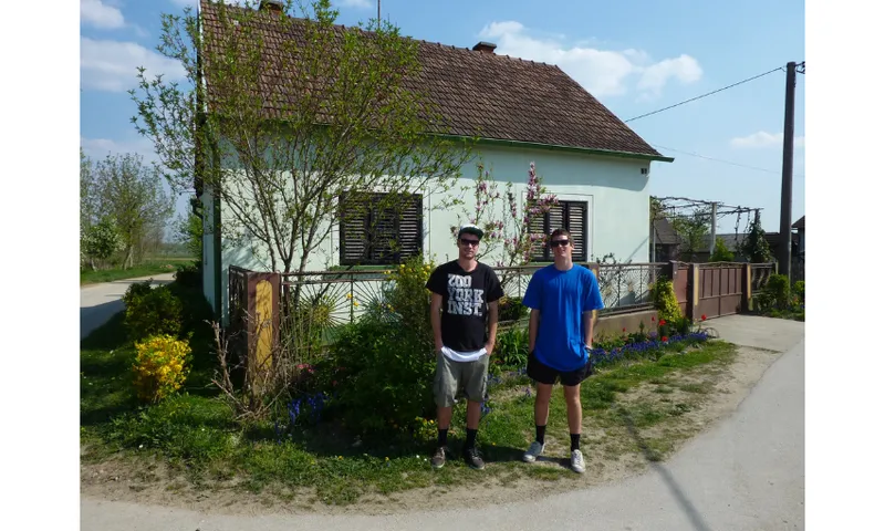 Two teenaged boys standing in front of a small house.