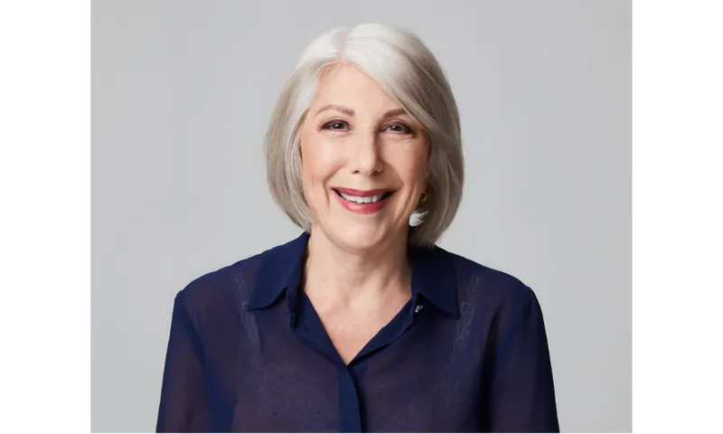 A photograph of an older woman with silver hair, smiling and wearing lipstick and a dark coloured blouse.