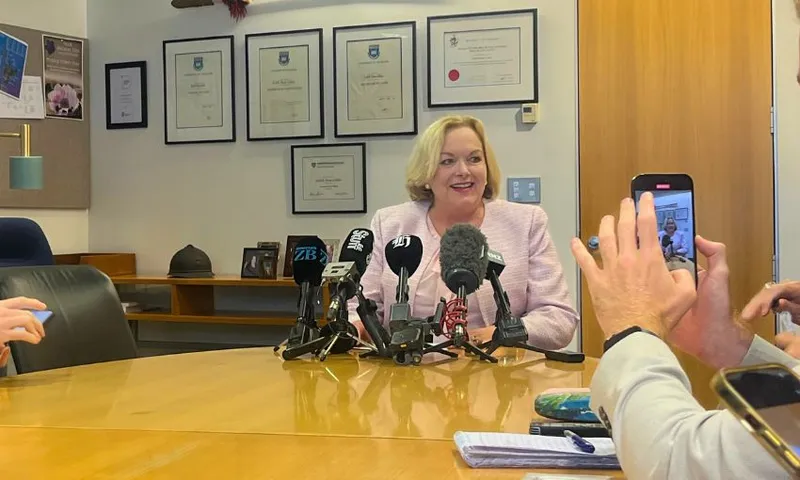 Judith Collins smiles while seated at a top of a long table.