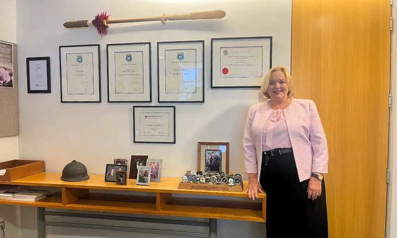 Judith Collins smiles while standing in her office, next to a wall of her framed degrees and gifted medals.