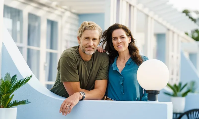 A blonde man wearing a green shirt and a woman with long brown hair and a teal coloured shop smile at the camera
