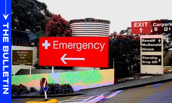 Large red "Emergency" sign with a white cross and arrow points left, near hospital entrance. Other signs direct to carpark, Ronald McDonald House, and Starship Drop Off. Trees and building structures are visible in the background.