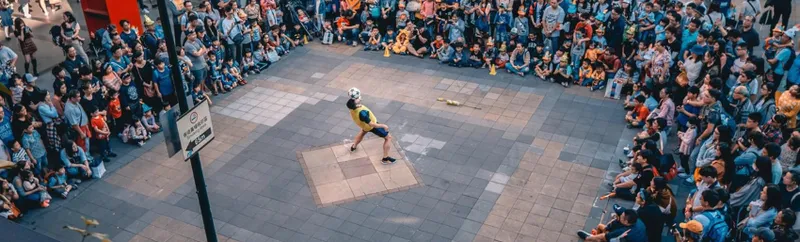 A photograph taken from high up looking over a street performer with a large crowd encircling them.