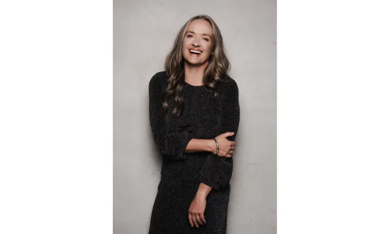 A photograph of actor and writer Elisabeth Easther. She has long hair and is wearing a long black, sparkly dress. She is smiling.