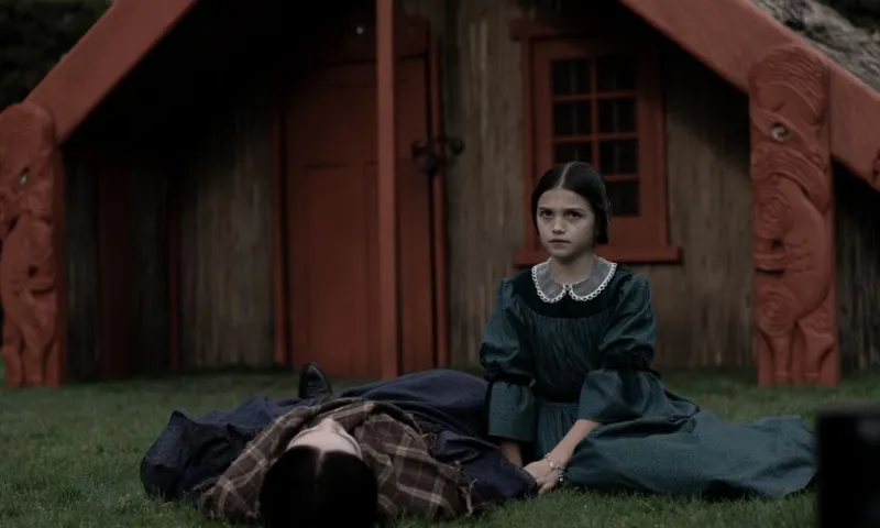 Maarama lies faceward in front of a wharenui, next to another younger girl.