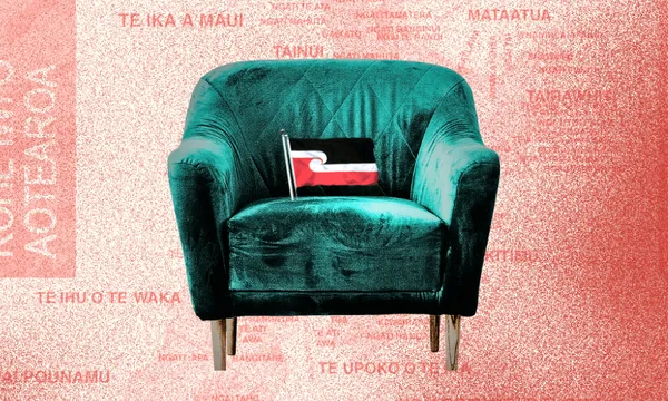 A green, velvet armchair with a small black, red, and white flag sits against a pink background covered in red text in te reo Māori.