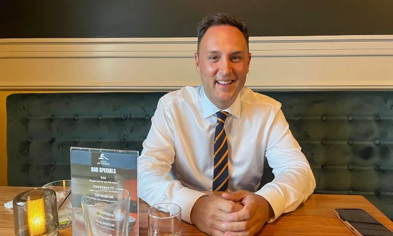 Shanan Halbert smiles while sitting at a bar table, his hands folded in front of him.