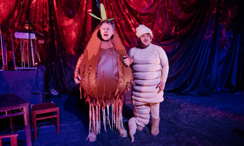 A photo of a stage set with two actors dressed as a worm and some kind of fruit.
