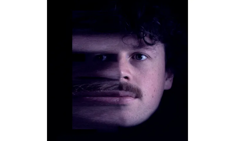 A close up photo of a young man's moustachioed face; the left side is blurring as if moving.