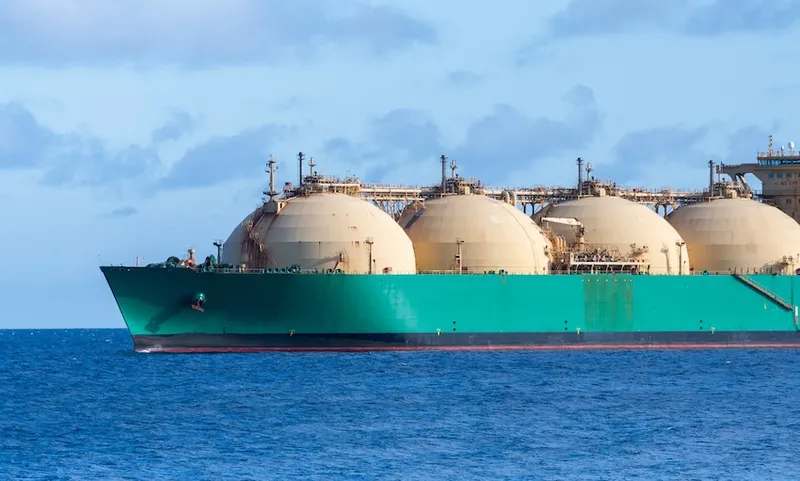 a shipping container that is green on the deep blue see with spherical containers on it looking ultra-industrial