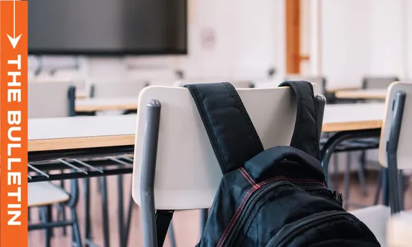 A black backpack hangs on the back of a classroom chair. Empty desks and chairs fill the room. An orange vertical banner on the left reads "The Bulletin.