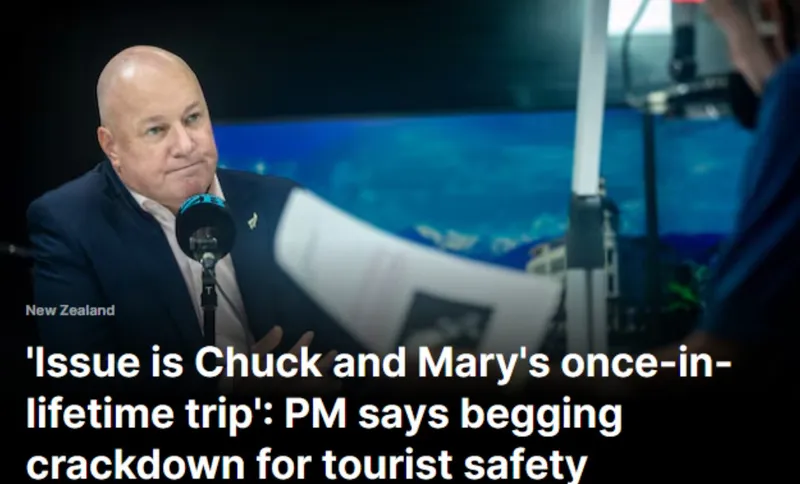 A man in a suit sits at a radio studio desk with a microphone, speaking to someone off-camera. The headline below discusses a Prime Minister addressing tourist safety and begging in New Zealand.