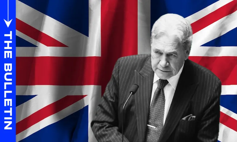 A man in a suit speaks at a podium in front of a large British flag; the left side has a blue vertical banner with the words "THE BULLETIN" in white text.