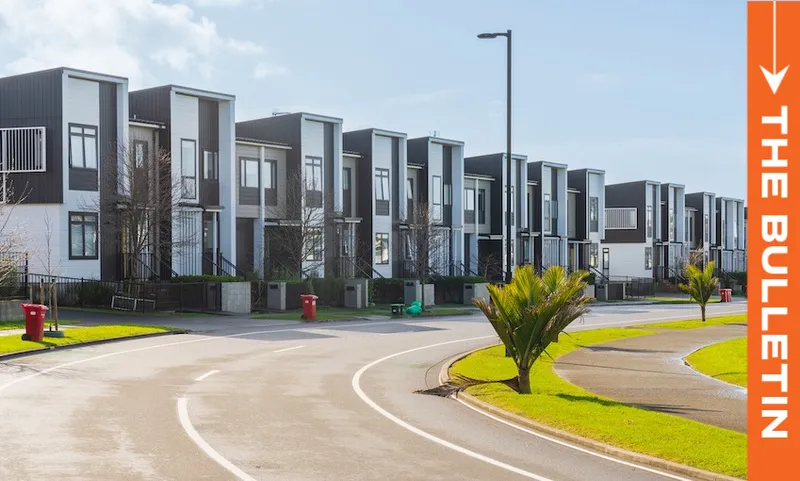 A row of modern, two-story townhouses lines a curved suburban street with green lawns, small palm trees, and red rubbish bins. A bright orange vertical banner reads "THE BULLETIN" on the right side of the image.