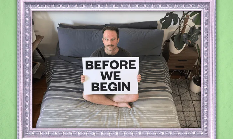 A man sits on a bed holding a sign that says before we begin