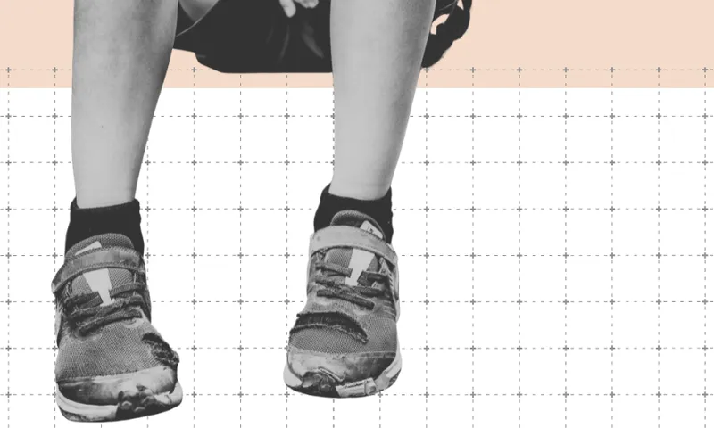 Black and white photo of a child’s lower legs and feet wearing sneakers, sitting on a swing with legs dangling. The background features a faint orange bar and a grid of dotted lines.